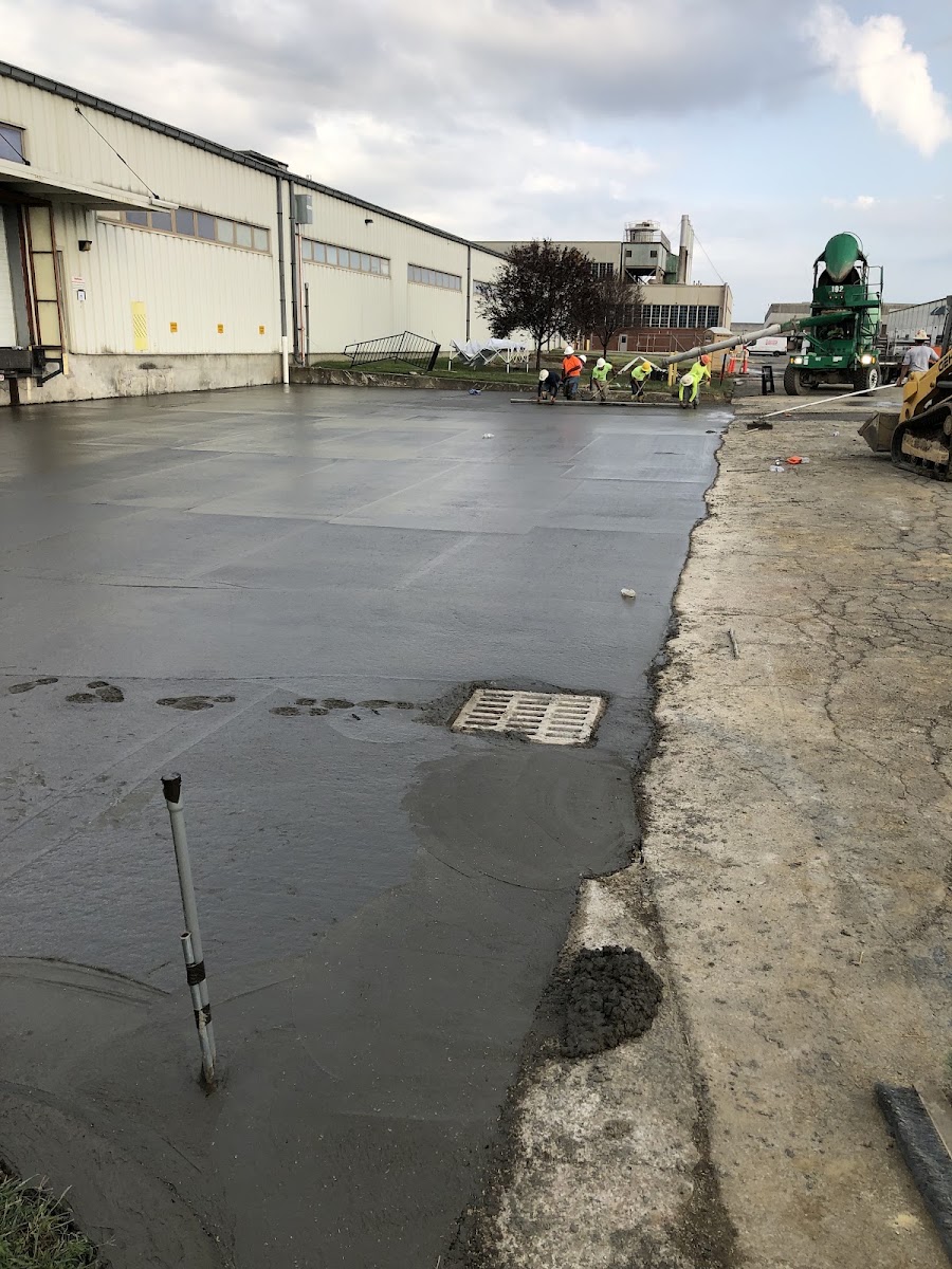 A large commercial concrete slab freshly poured, with a concrete mixer truck and crew finishing the surface