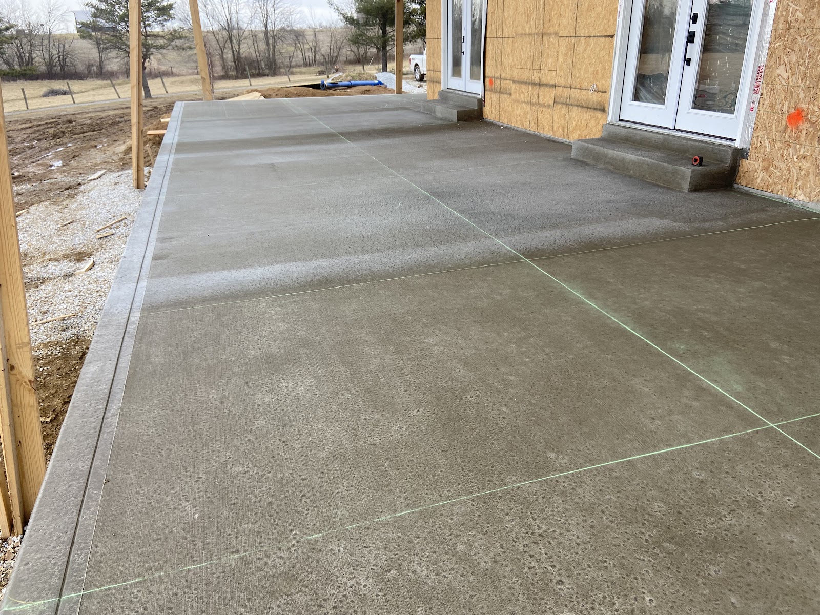 A large new-construction concrete patio slab poured behind a home under framing
