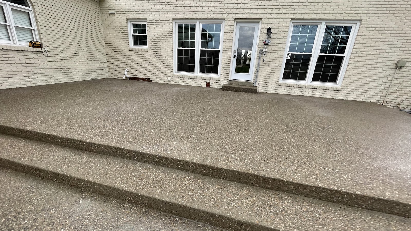 An exposed-aggregate concrete patio with steps against a brick house